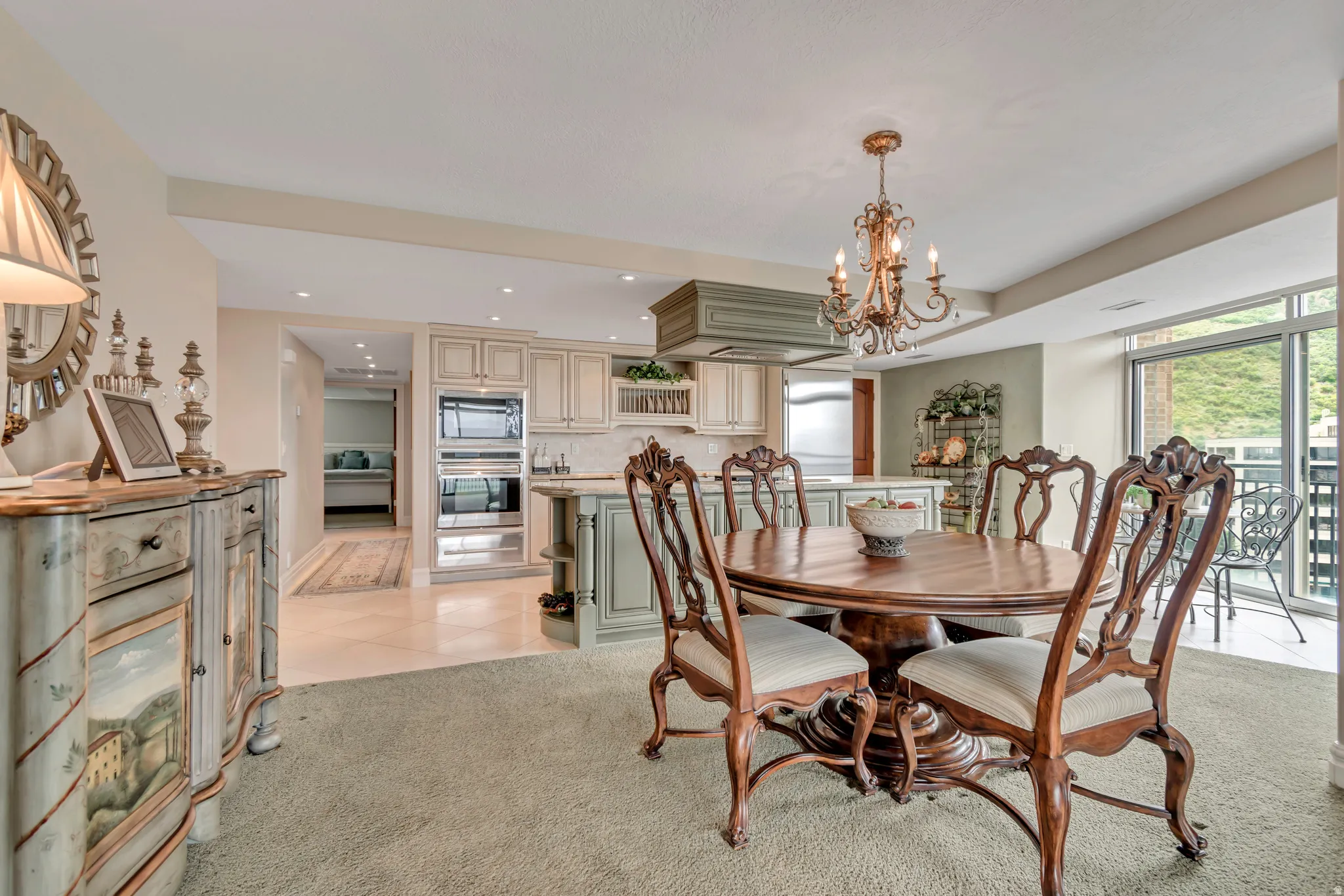 Spacious interior featuring a dining area with a chandelier, a kitchen with built-in appliances, and a balcony with a mountain backdrop