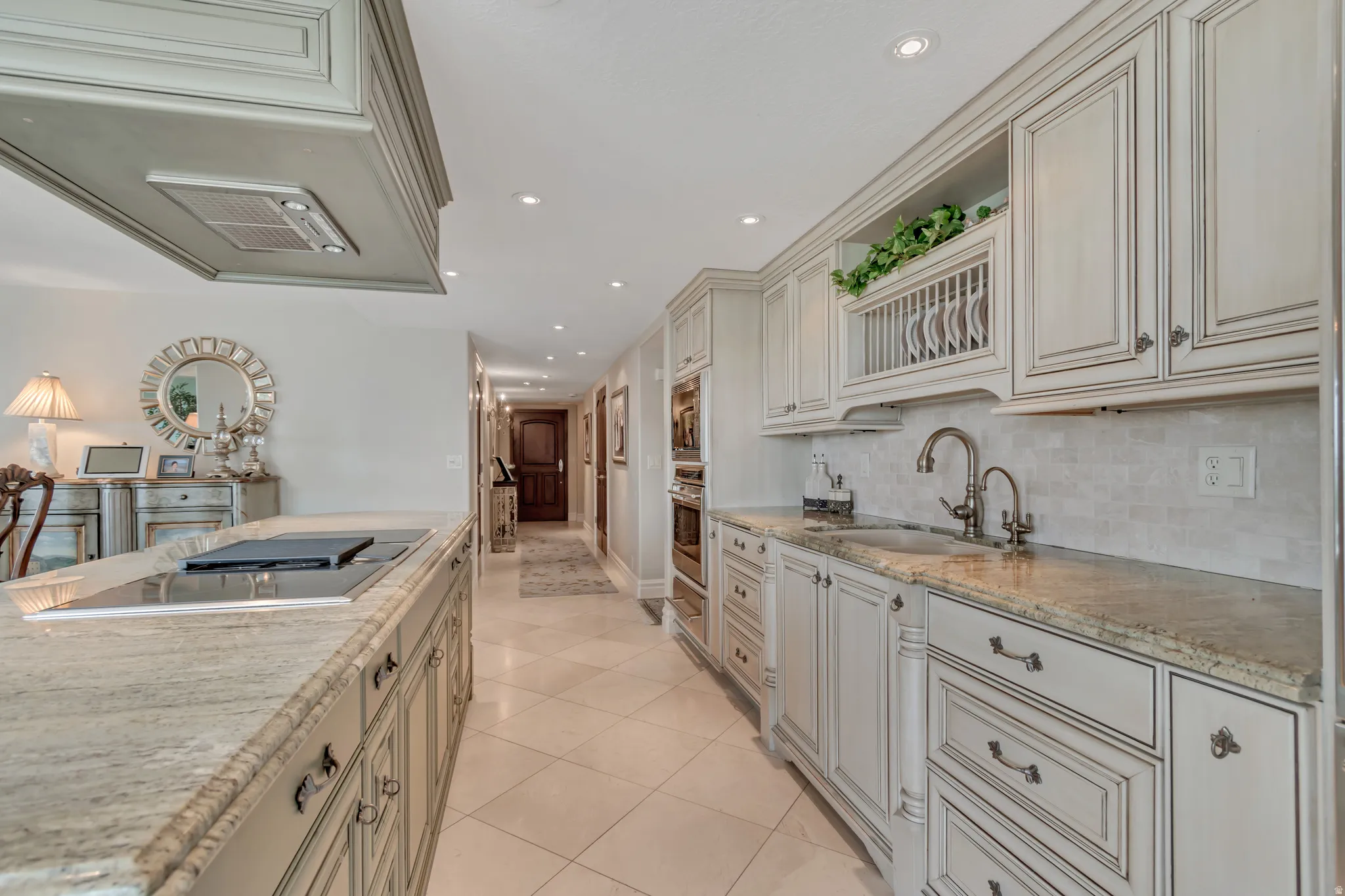 Gourmet kitchen featuring extensive cabinetry with decorative trim, granite countertops, an undermount sink with a gooseneck faucet, a built-in cooktop, and an integrated oven