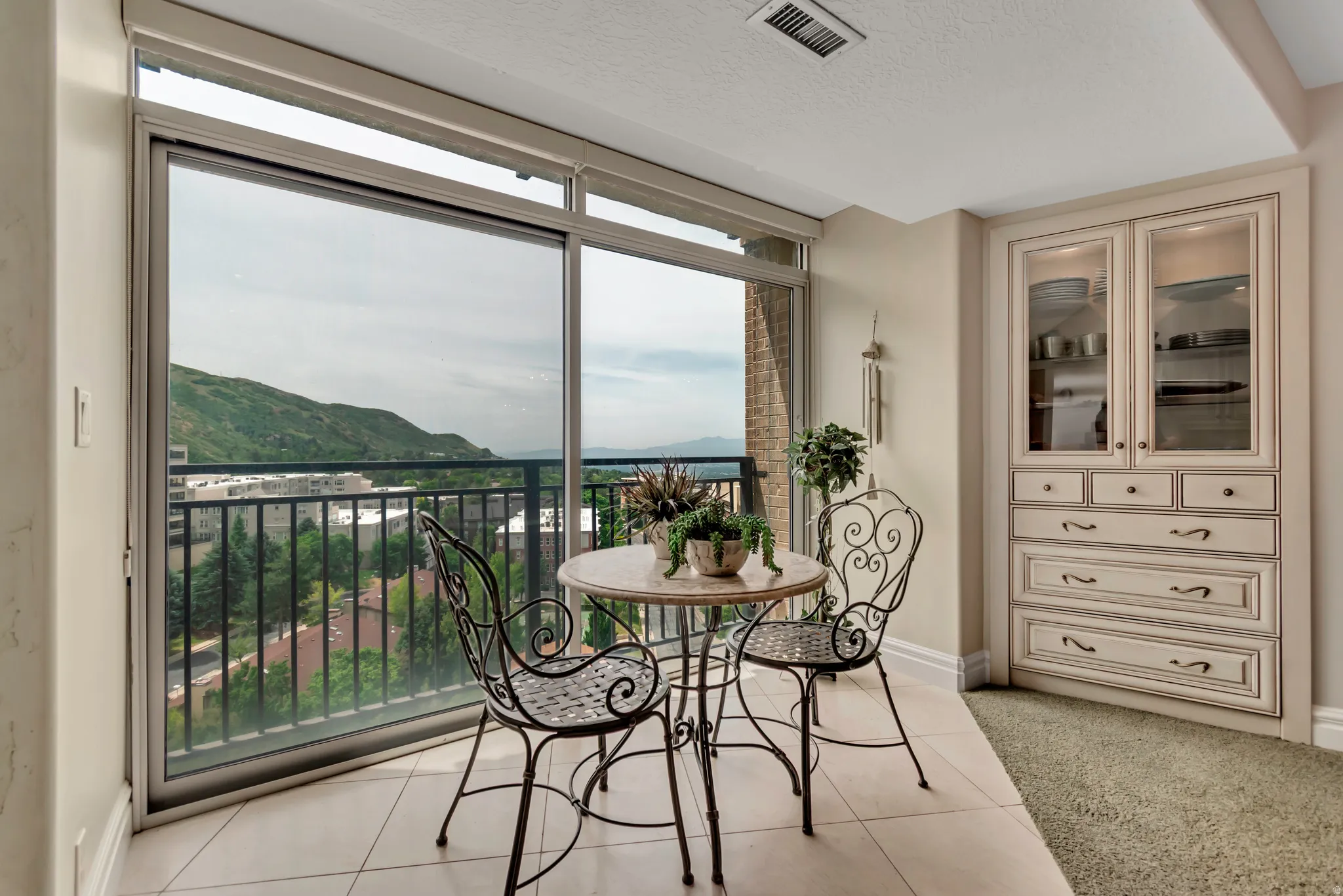 Sliding glass doors opening to a balcony with metal railing, featuring tile flooring and built-in cabinetry with glass display doors and lower drawers