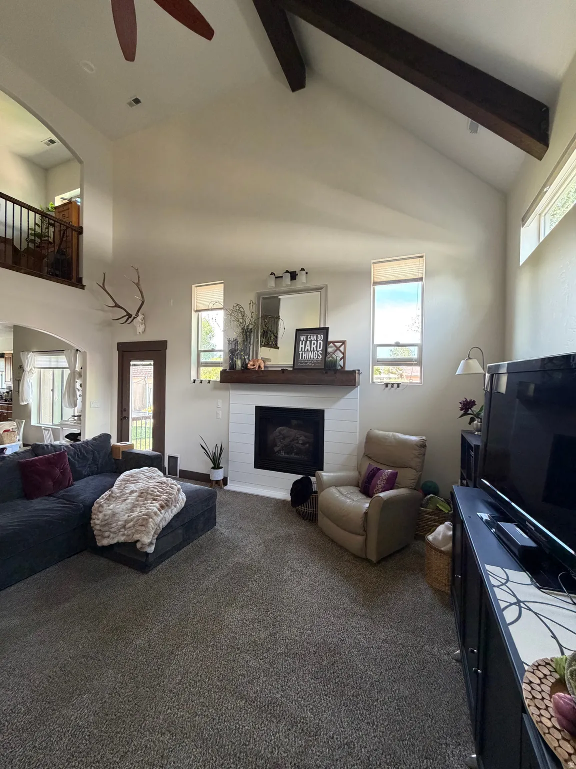 Living area featuring a vaulted ceiling with exposed wood beams, a ceiling fan, and a fireplace with a shiplap surround and wood mantel
