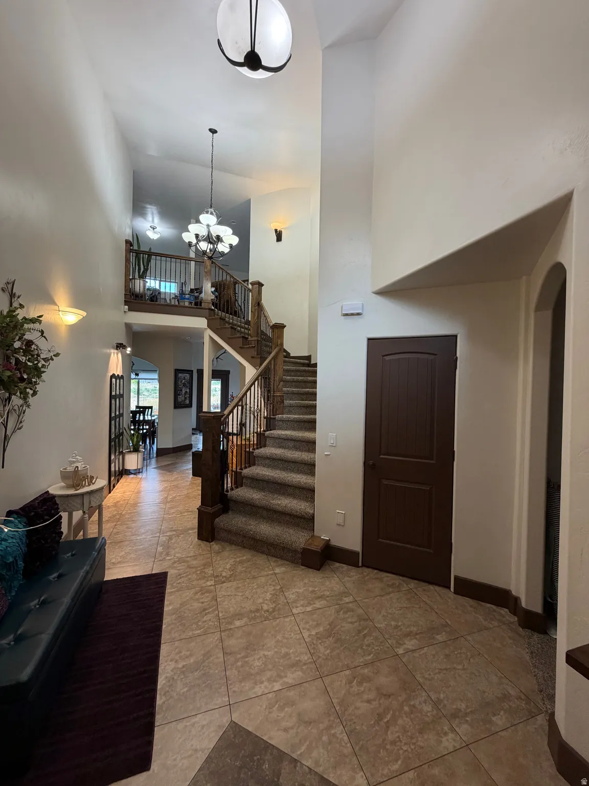 Two-story foyer featuring tile flooring, a carpeted staircase with wood newel posts and iron balusters, and a tiered chandelier