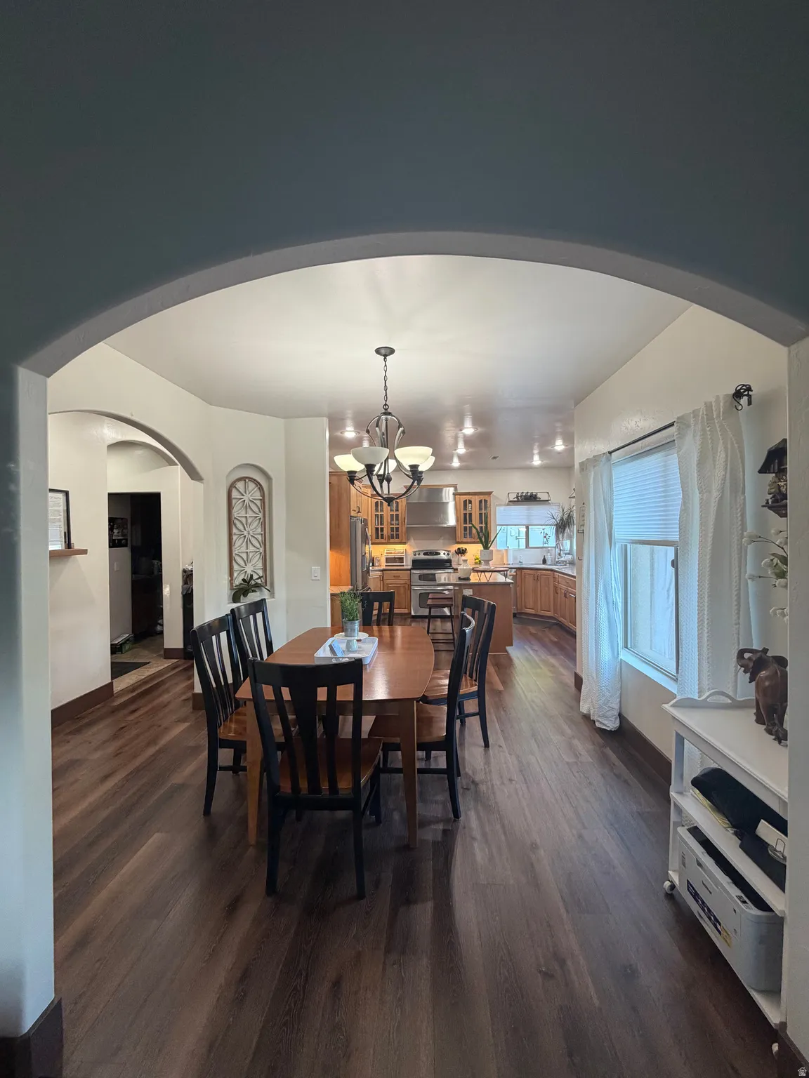 Expansive dining area featuring wood-finish flooring, a decorative chandelier, and an arched entryway