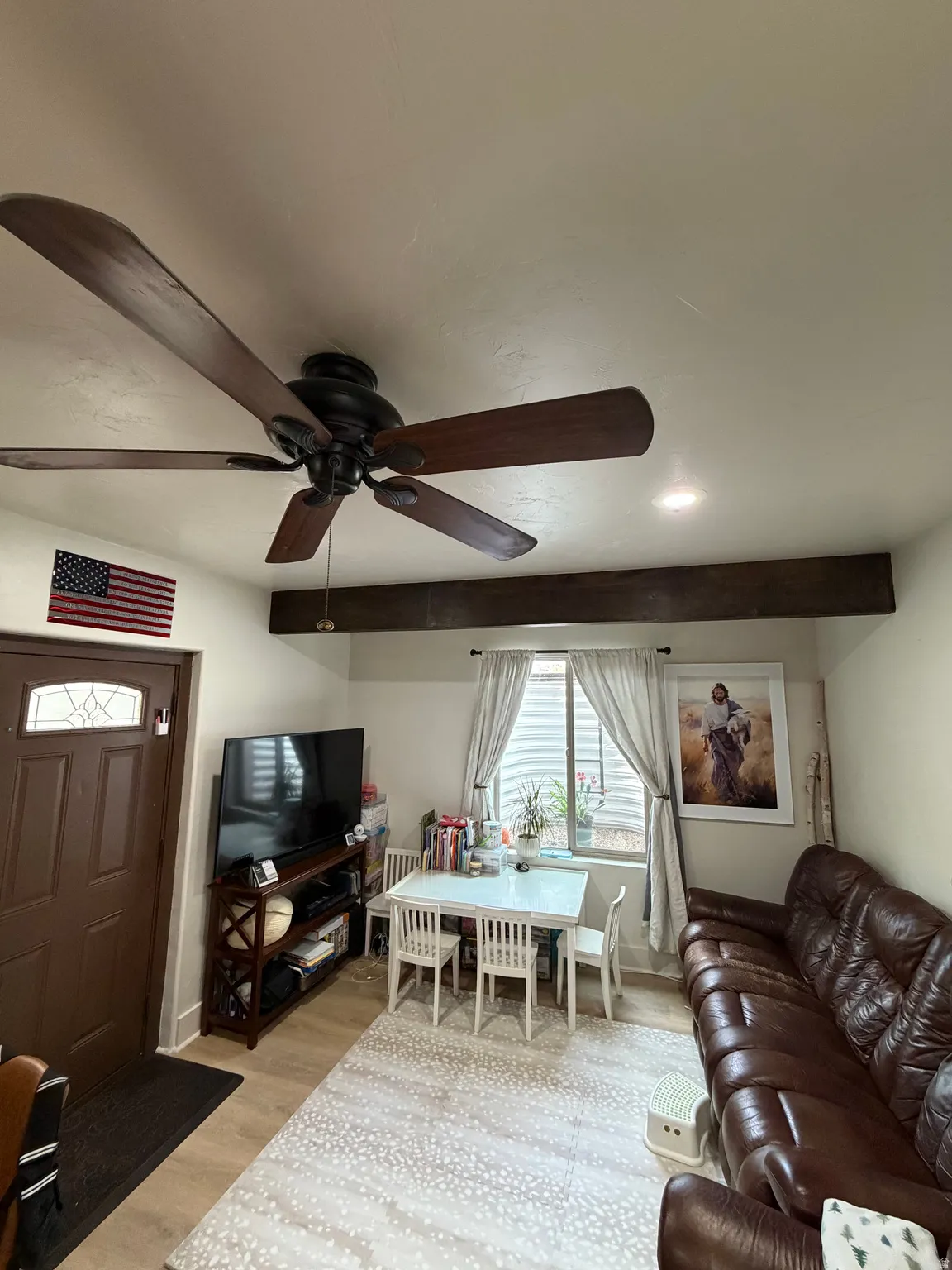 Spacious living area featuring a dark wood-finish ceiling fan, recessed lighting, and a prominent decorative beam