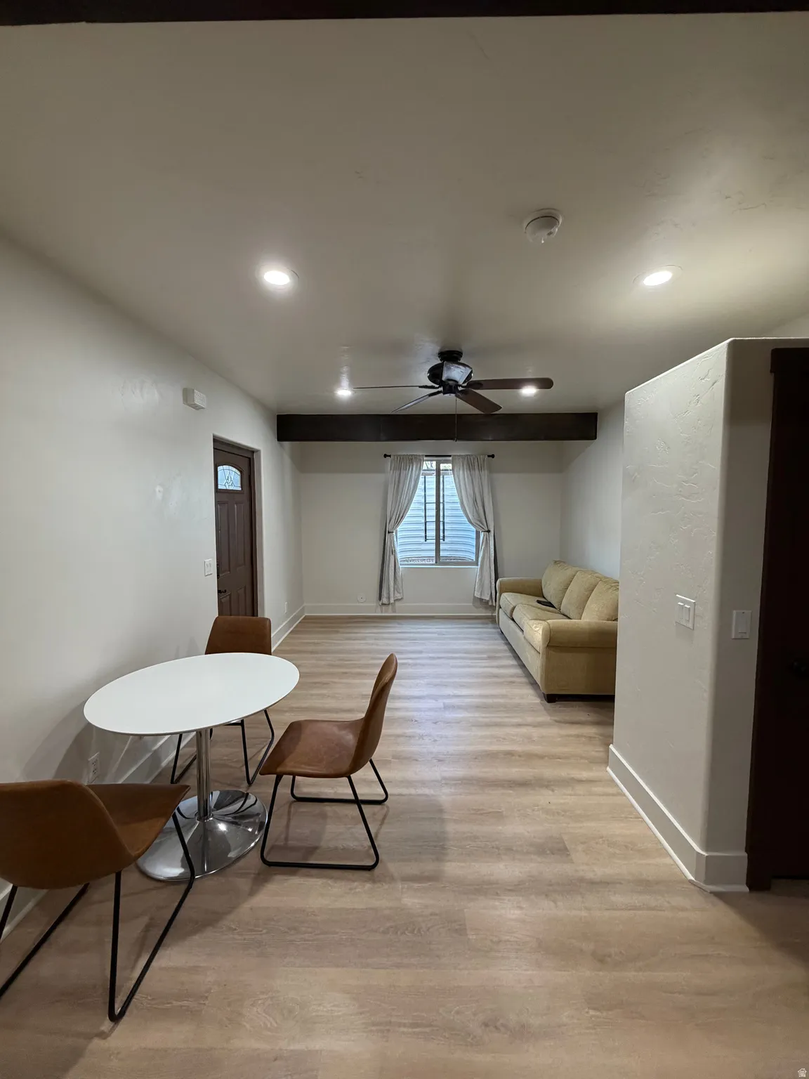 Spacious open-concept room featuring wood-finish flooring, recessed lighting, and a dark wood ceiling beam