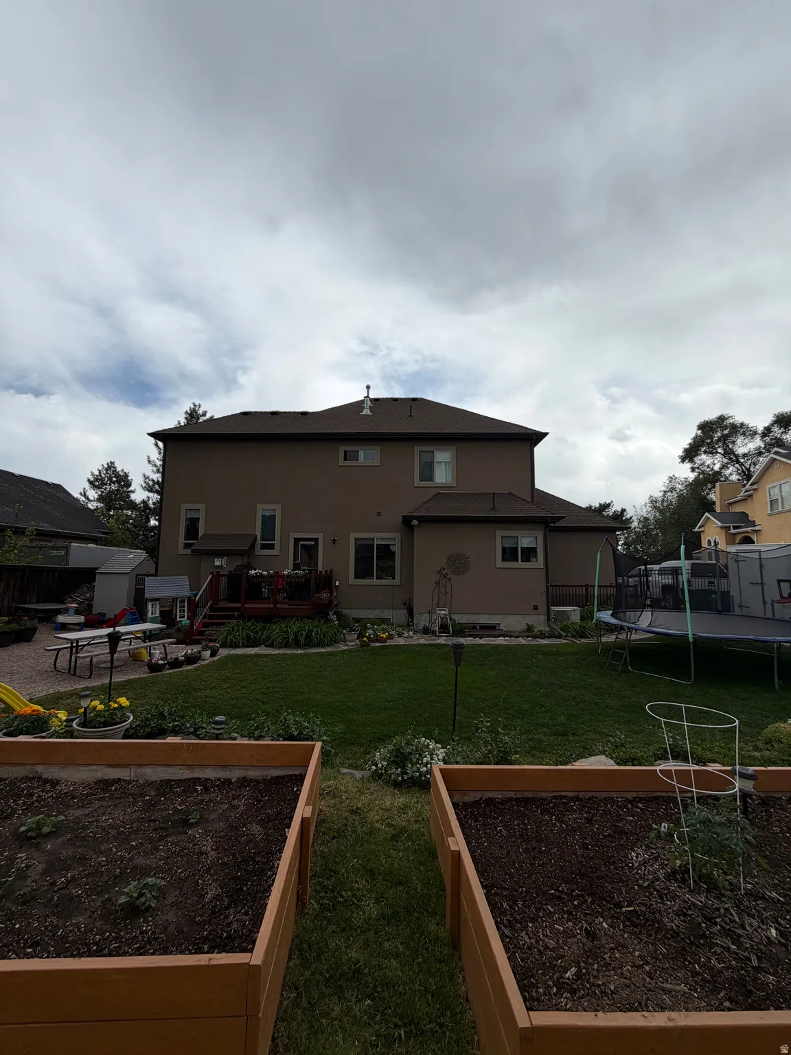 Expansive backyard featuring a manicured lawn, a multi-level wood deck, and multiple raised garden beds