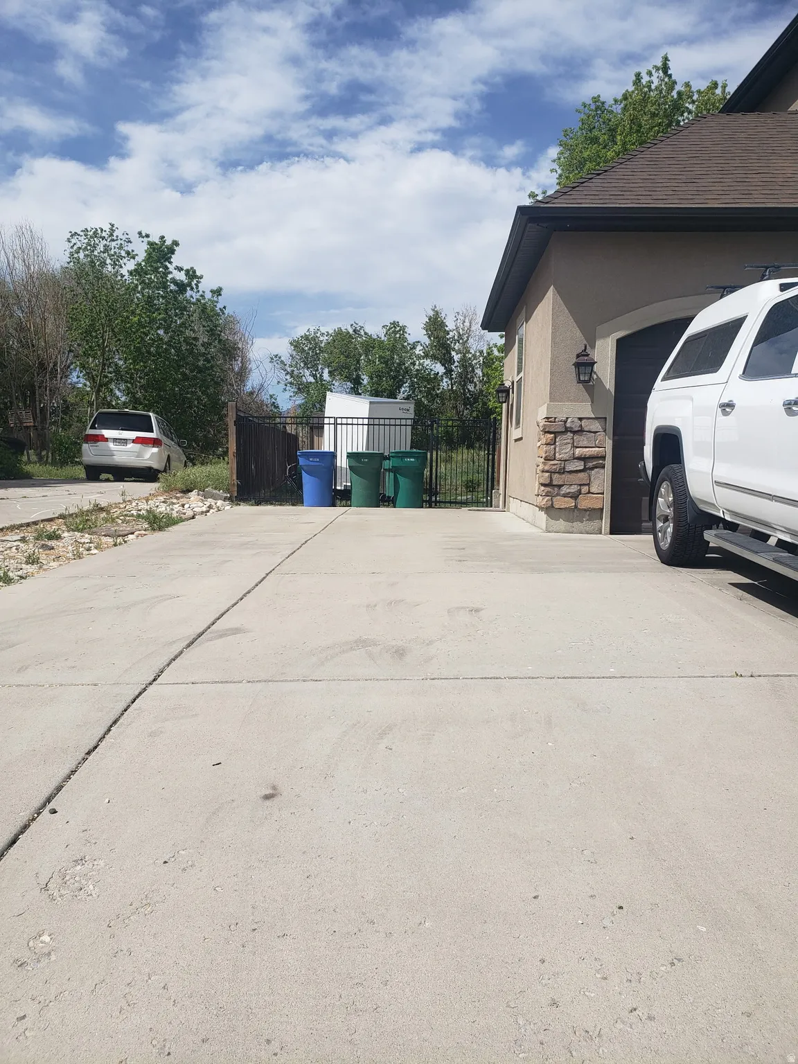 Paved concrete driveway providing ample parking, complemented by a stucco exterior with stone accents and a dark roof