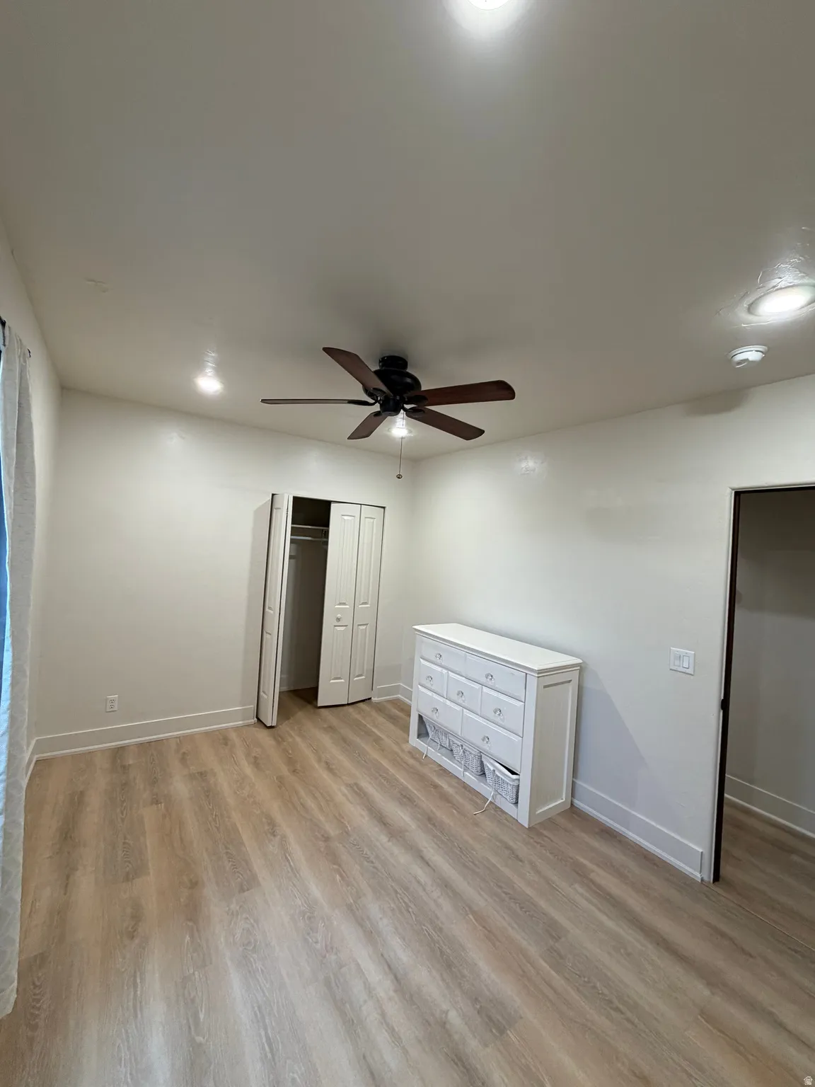 Spacious room featuring wood-finish flooring, white baseboards, and bright recessed lighting