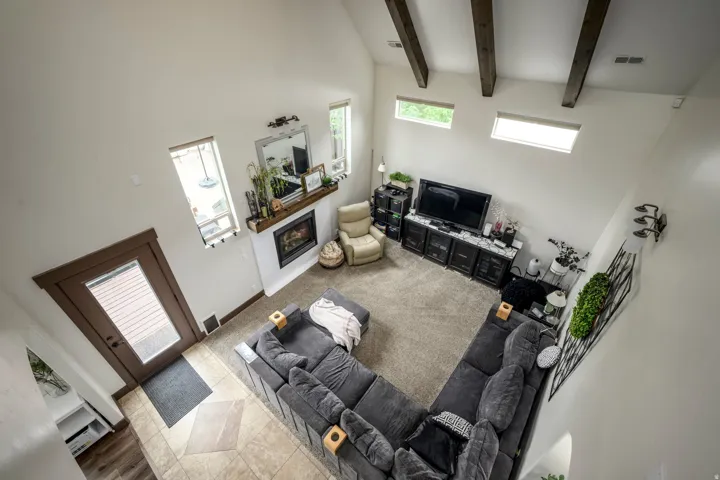 Vaulted ceiling with exposed wood beams, white fireplace with wood mantel, multiple windows, and tile flooring at entry