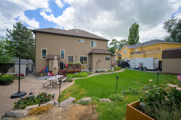 Expansive backyard with a manicured lawn, gravel patio, and multiple storage sheds