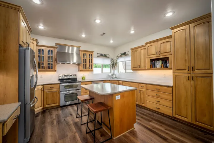 Kitchen featuring wood cabinetry, stainless steel appliances, an island with countertop seating, recessed lighting, and wood-finish flooring