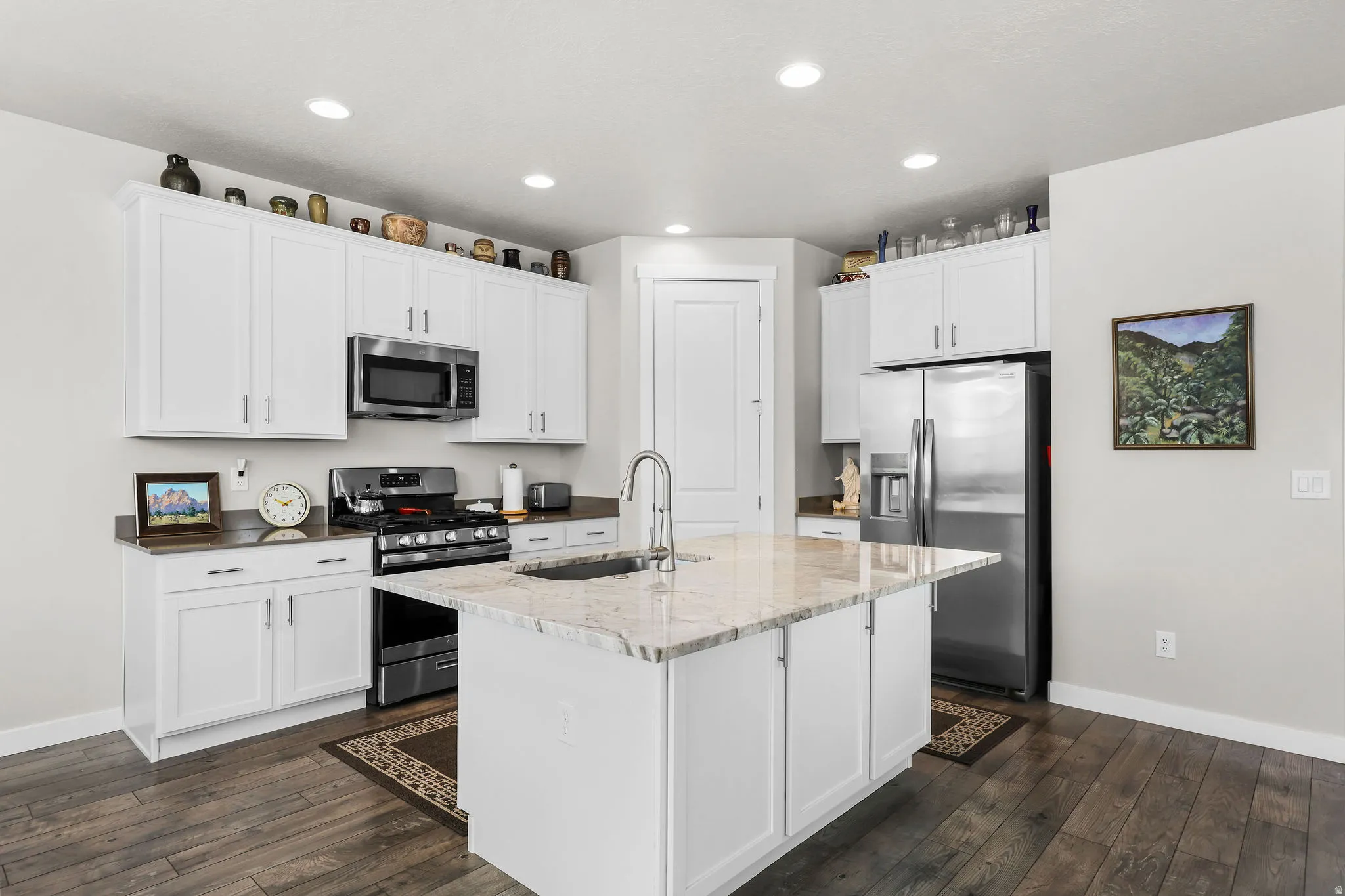 Kitchen featuring a central island with an undermount sink, white cabinetry with silver hardware, stainless steel appliances, dark wood-finish flooring, and recessed lighting