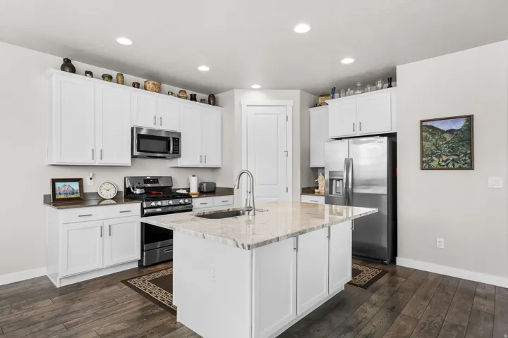 Kitchen featuring a central island with an undermount sink, white cabinetry with silver hardware, stainless steel appliances, dark wood-finish flooring, and recessed lighting