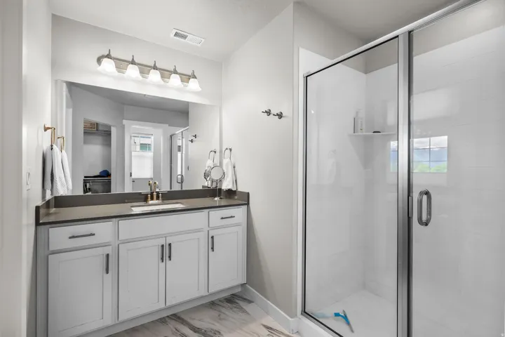 Bathroom featuring a glass-enclosed shower, a vanity with a dark countertop, white shaker-style cabinetry, and a large mirror with overhead lighting