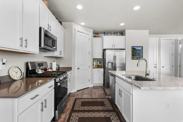 Contemporary kitchen featuring white cabinetry, stainless steel appliances, a center island with sink, quartz countertops, and wood-finish flooring