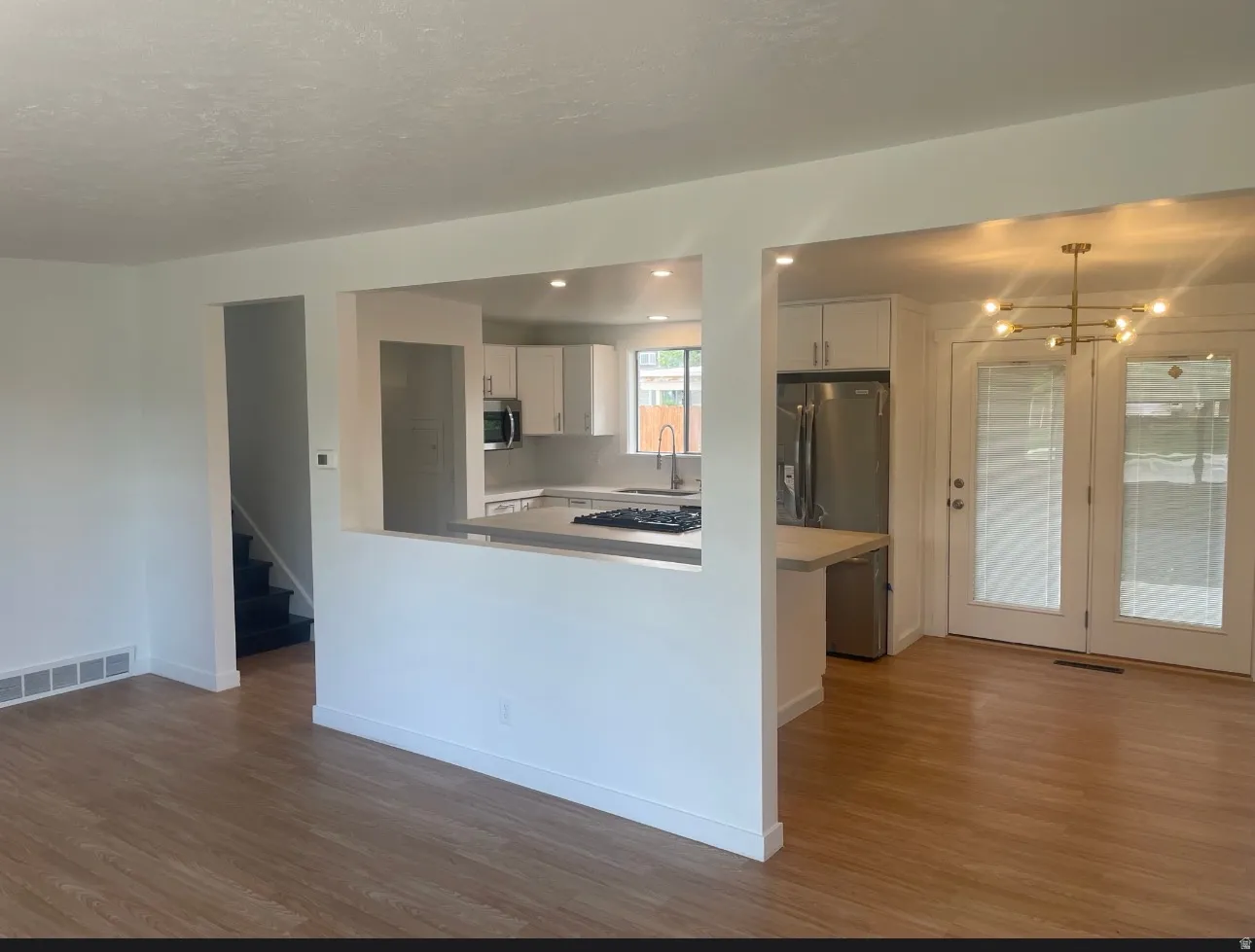 Open concept living area with wood-finish flooring, white walls, and a partial wall separating the kitchen