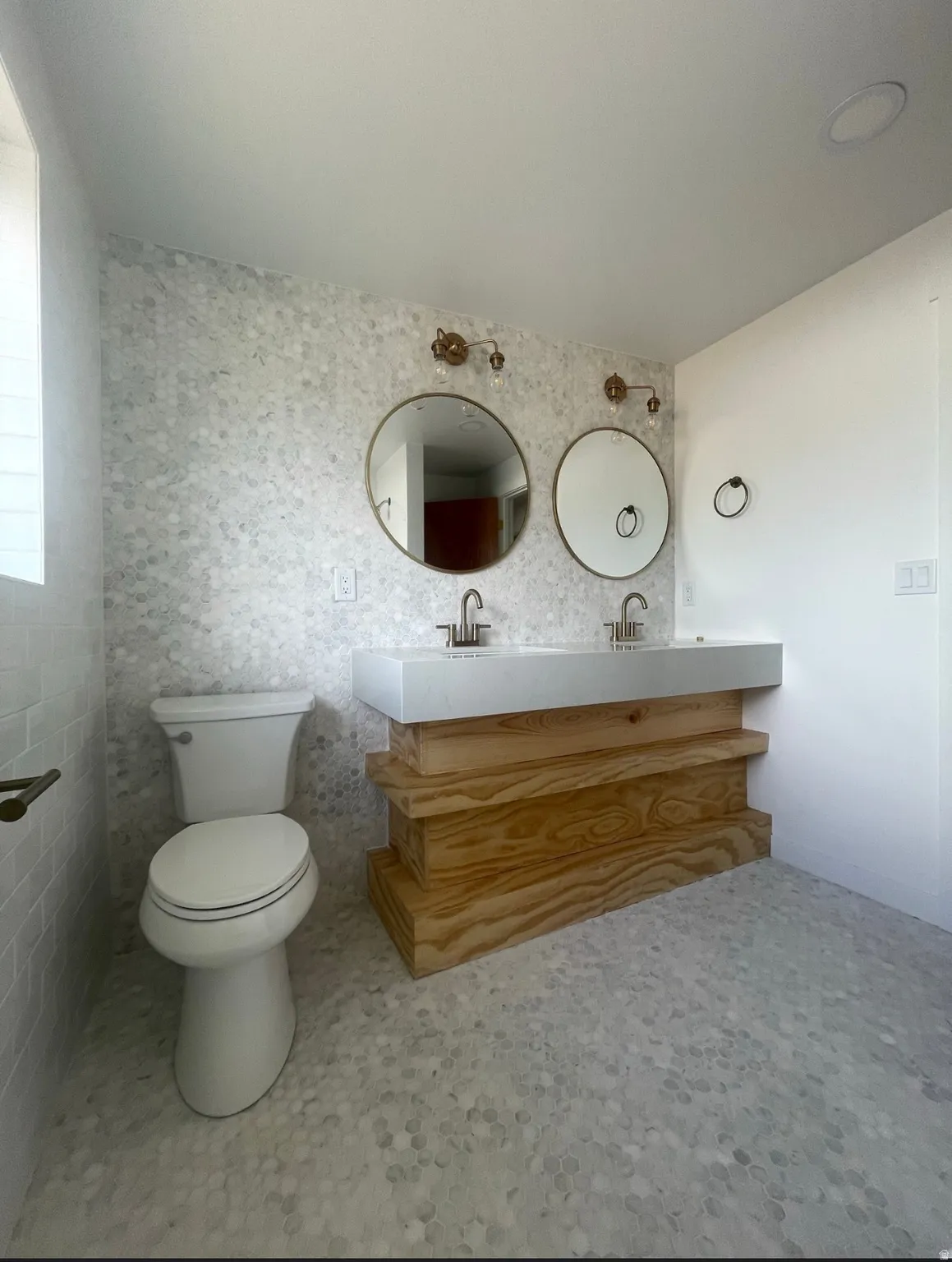 Bathroom featuring a dual vanity with a light wood-finish base, dual circular mirrors, and a tile accent wall