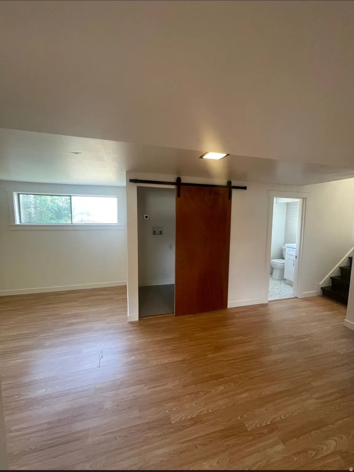 Spacious interior room featuring wood-finish flooring, a contemporary barn door, a recessed horizontal window, and a square ceiling light fixture