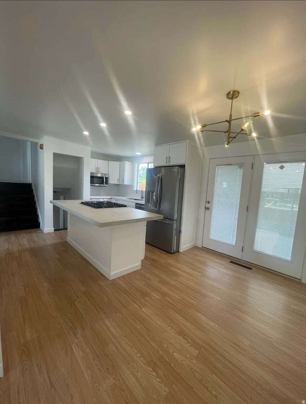 Open-concept kitchen featuring an island with cooktop, stainless steel appliances, white cabinetry, and wood-finish flooring