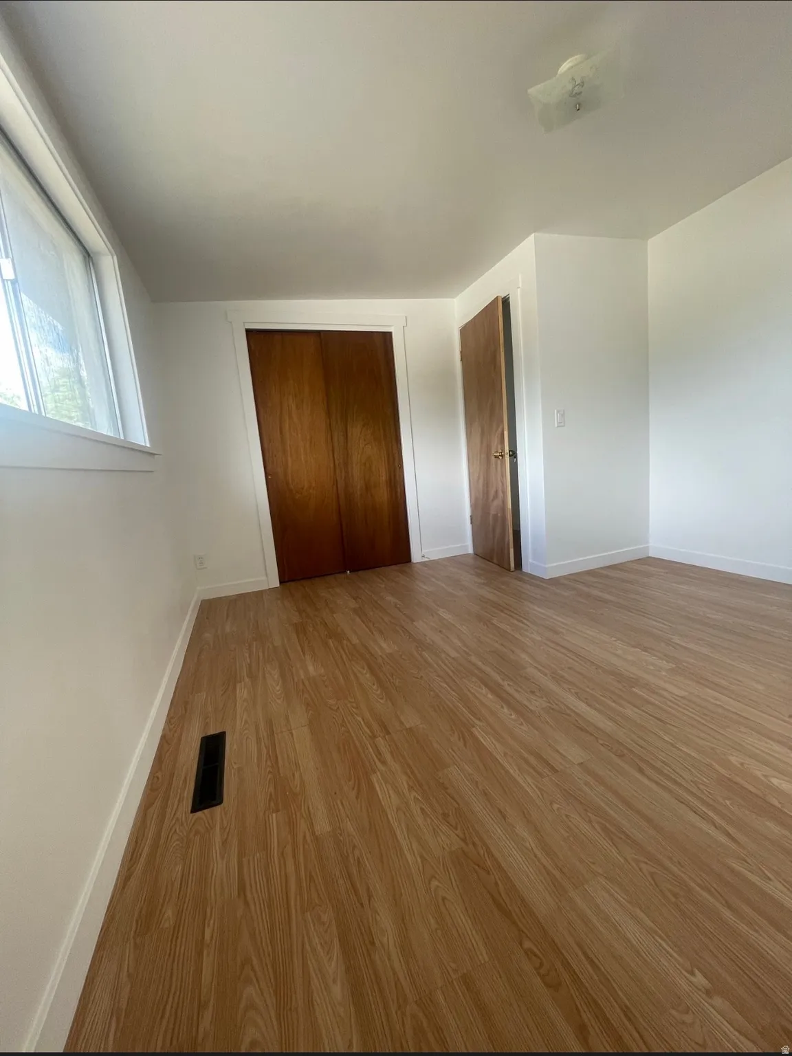 Spacious room featuring wood-finish flooring, white baseboards, and a window
