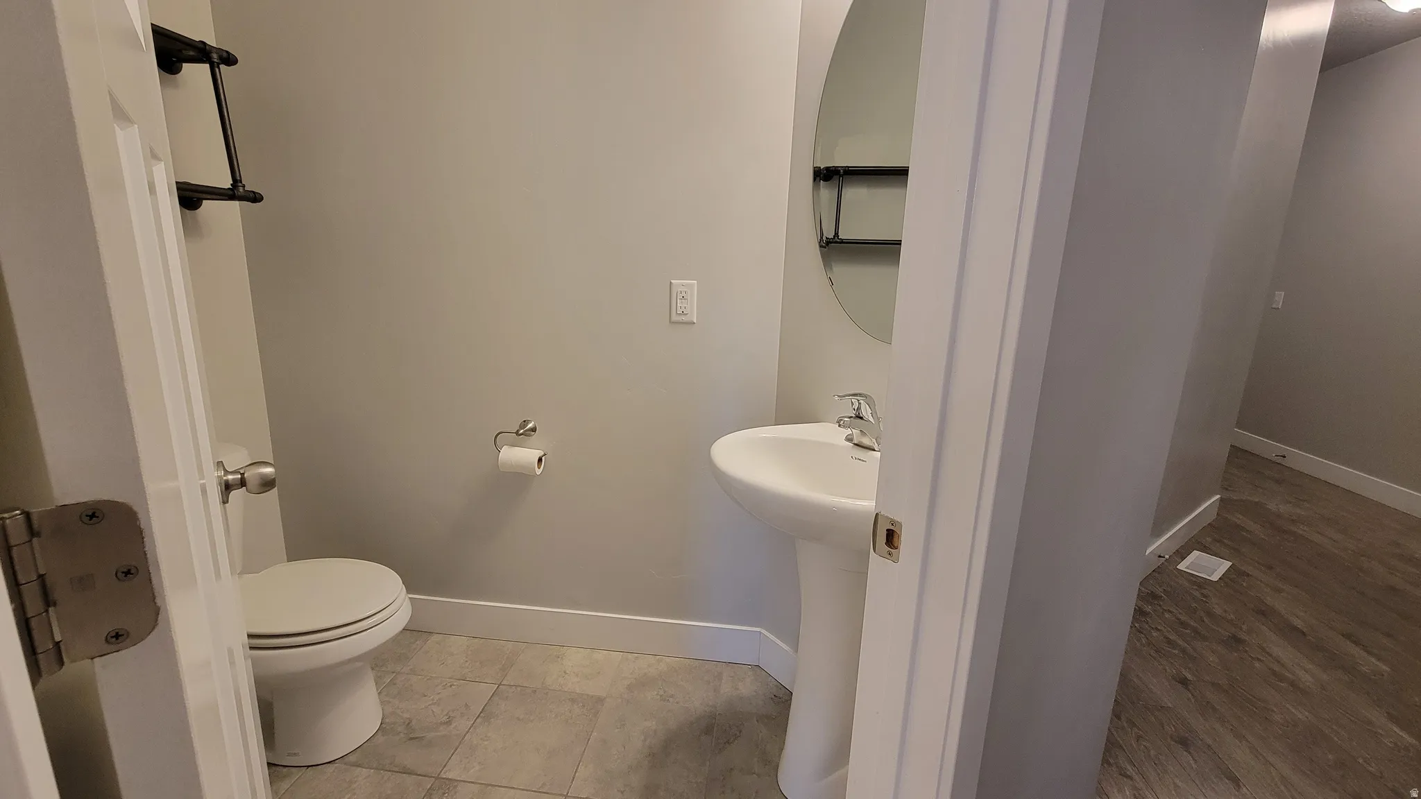 Compact powder room featuring a pedestal sink, round mirror, and tile flooring
