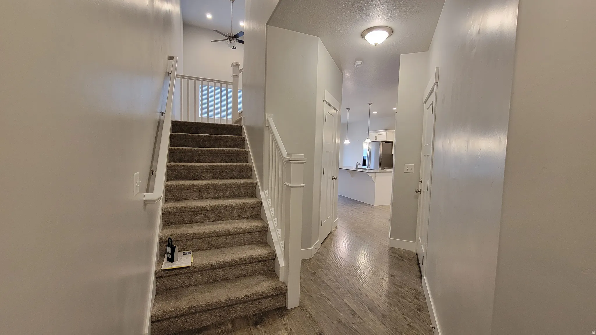 Carpeted staircase with white balusters leading to a vaulted ceiling with a ceiling fan