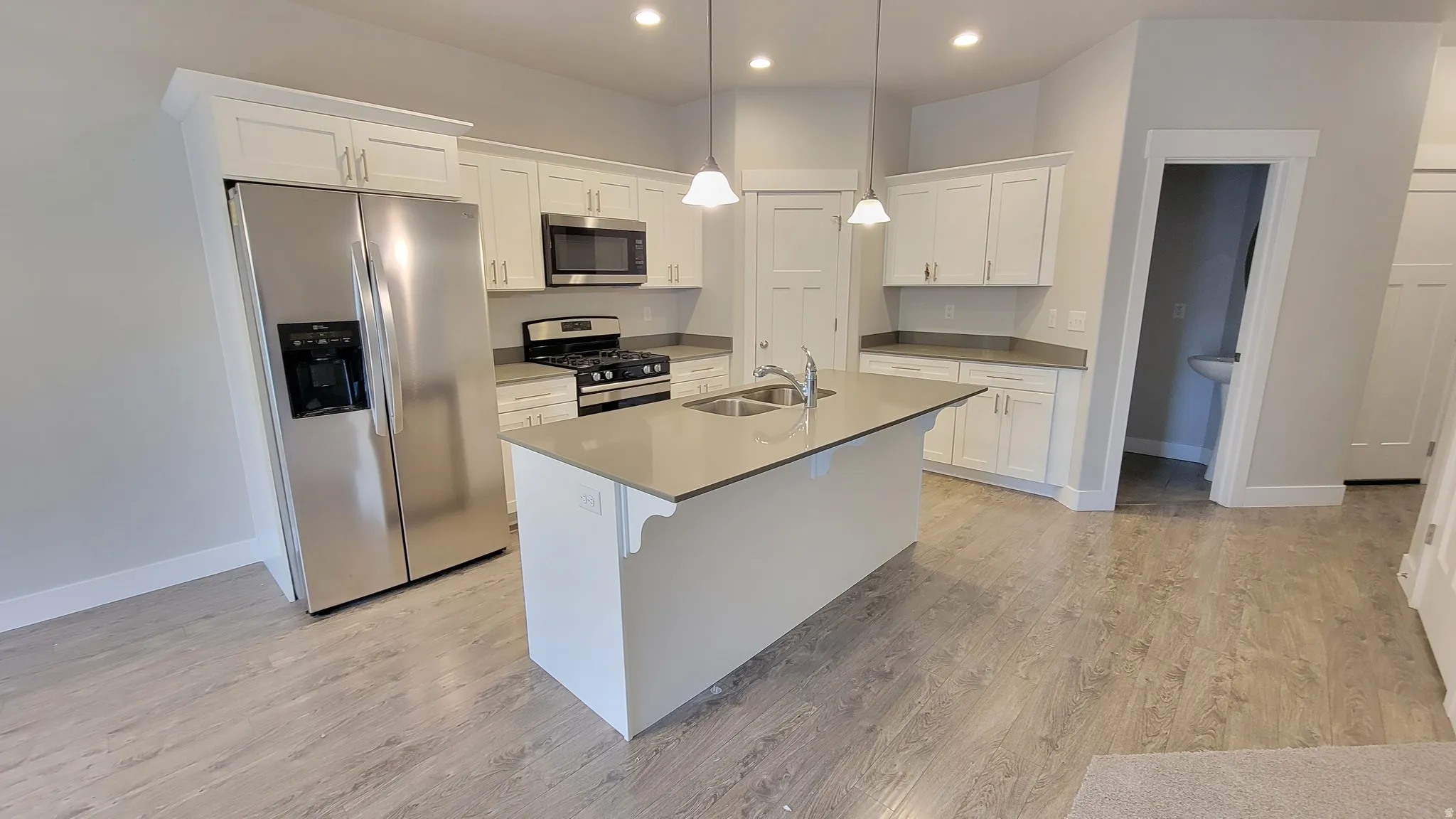Kitchen featuring a central island with dual sinks, light-toned countertops, white cabinetry, stainless steel appliances, and wood-finish flooring