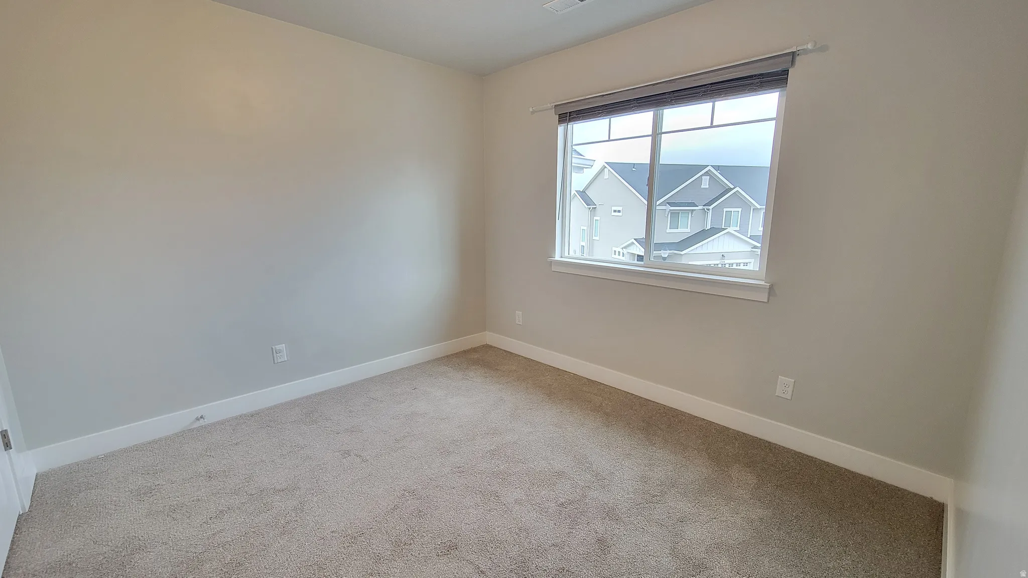 Carpeted room featuring light gray walls, white trim, and a window with a roller shade