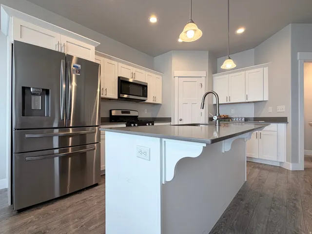 Modern kitchen featuring a central island with a sink and faucet, white cabinetry, stainless steel appliances, and wood-finish flooring
