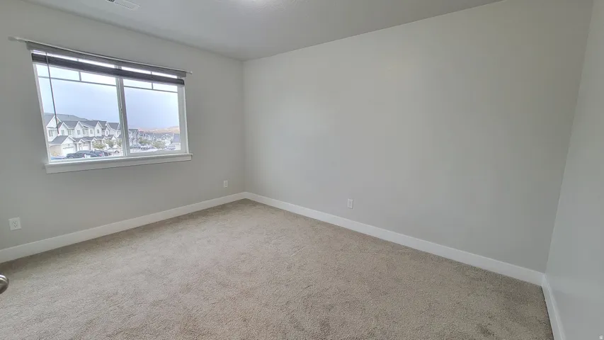 Carpeted room featuring a large window with roll-up blinds, neutral paint tones, and white baseboards