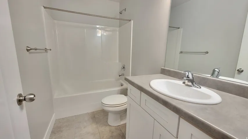 Bathroom featuring a white vanity with a gray countertop, an integrated sink with chrome faucet, a large mirror, and a combined tub and shower unit with a chrome shower rod