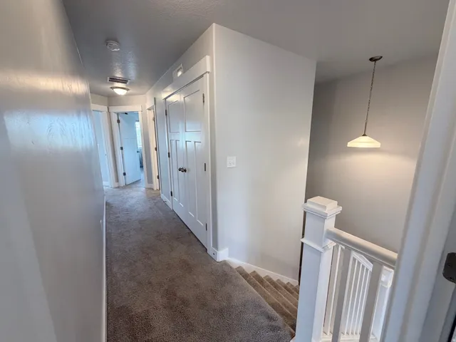 Carpeted hallway featuring multiple white paneled doors with dark hardware, recessed lighting, and a traditional white baluster staircase