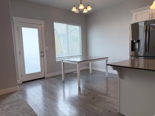 Spacious dining area featuring wood-finish flooring, a contemporary chandelier, and a frosted glass-paneled door