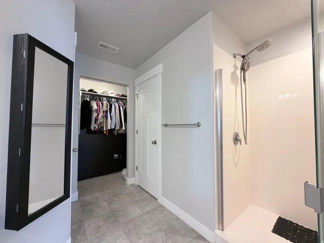Tiled flooring throughout this space features a walk-in shower with a glass enclosure, a mounted showerhead with an additional handheld sprayer, and a recessed walk-in closet with built-in shelving