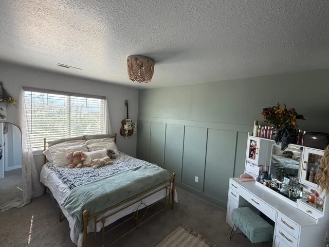 Bedroom featuring a built-in board and batten accent wall, window with horizontal blinds, and a ceiling-mounted light fixture