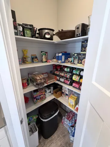 Corner pantry featuring extensive white shelving, recessed lighting, and wood-finish flooring