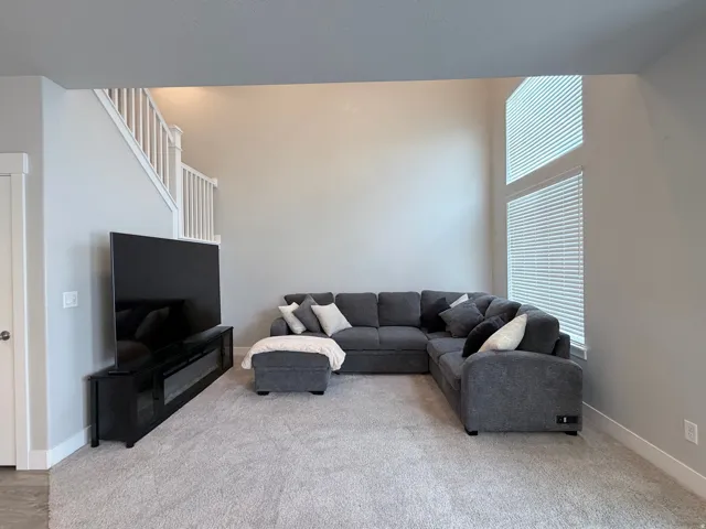Spacious living area featuring high ceilings, light gray wall tones, and carpet flooring
