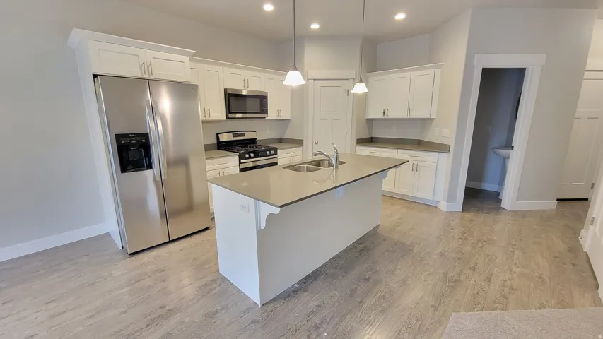 Kitchen featuring a central island with dual sinks, light-toned countertops, white cabinetry, stainless steel appliances, and wood-finish flooring