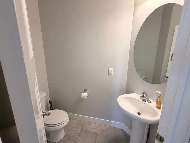 Powder room featuring a pedestal sink, oval mirror, gray wall paint, and tile flooring