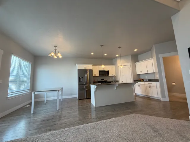 Open-concept living space featuring wood-finish flooring, a kitchen island with pendant lighting, white cabinetry, recessed lighting, and a stainless steel refrigerator