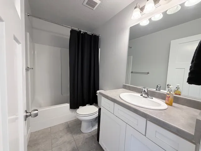 Full bathroom featuring a white tub and shower combination, a single vanity with a white cabinet and grey countertop, a large wall-mounted mirror, and tile flooring