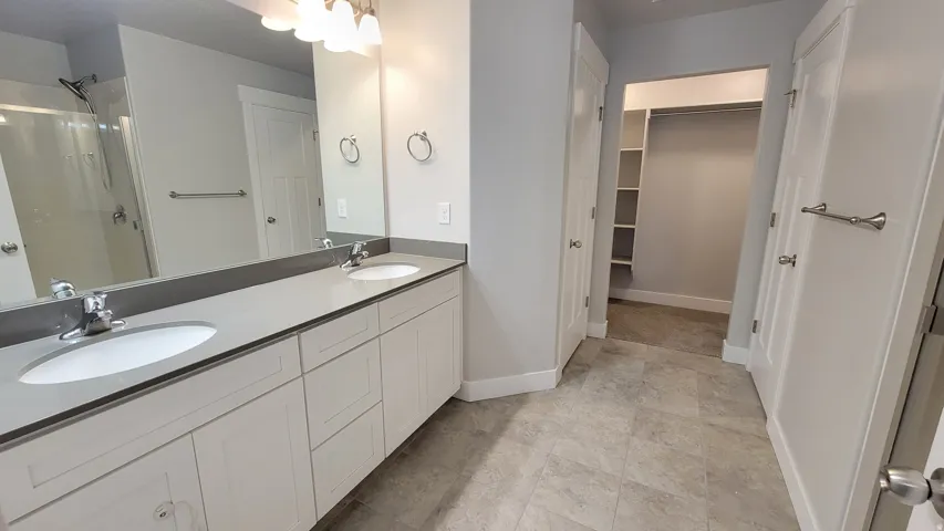 Bathroom featuring a dual vanity with light grey countertops, undermount sinks, and white shaker-style cabinetry