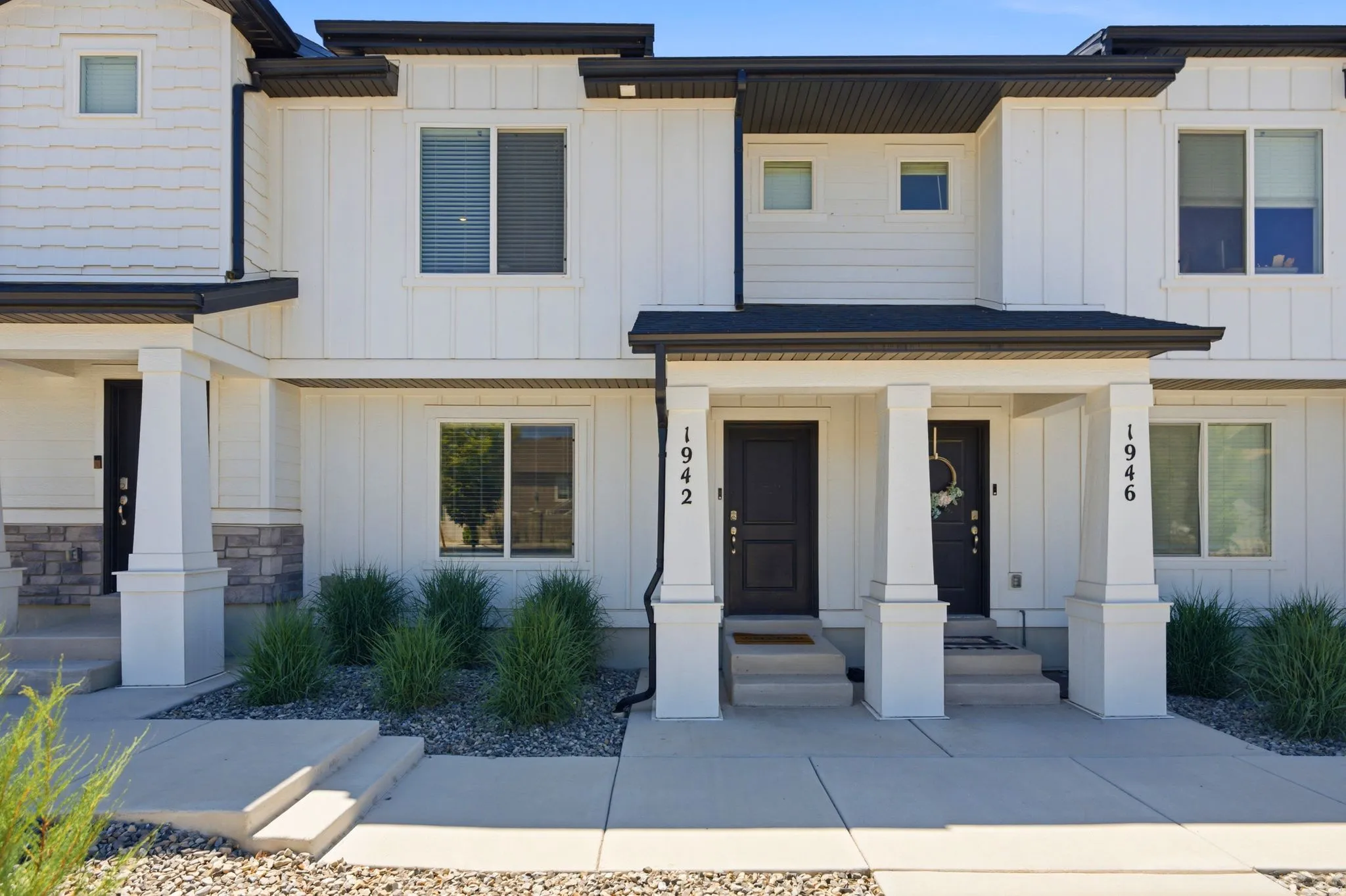 Contemporary townhome exterior with white board and batten siding, black trim, and a covered porch entry