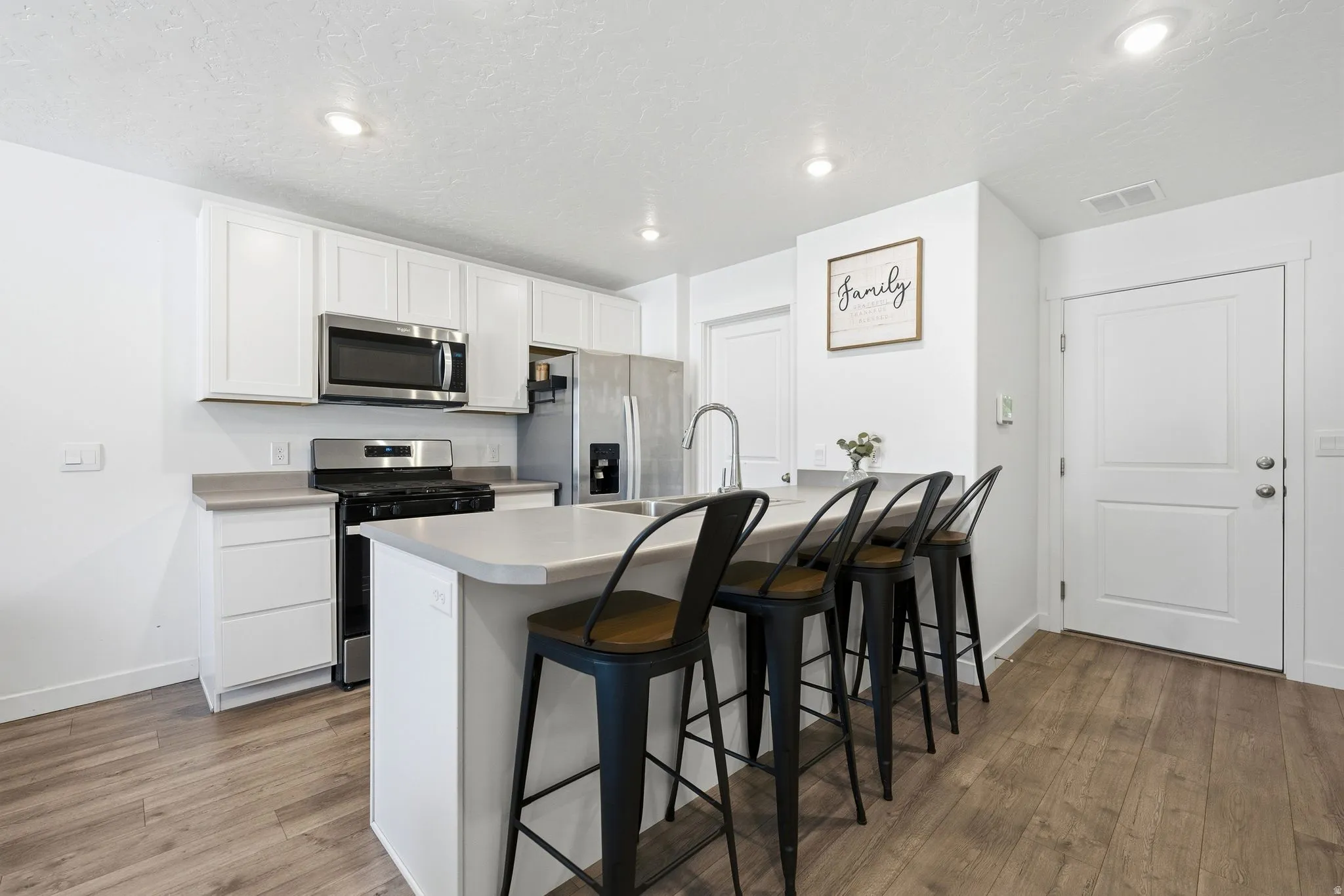 Modern kitchen featuring white cabinetry, stainless steel appliances, light-toned countertops, a kitchen island with seating, and wood-finish flooring