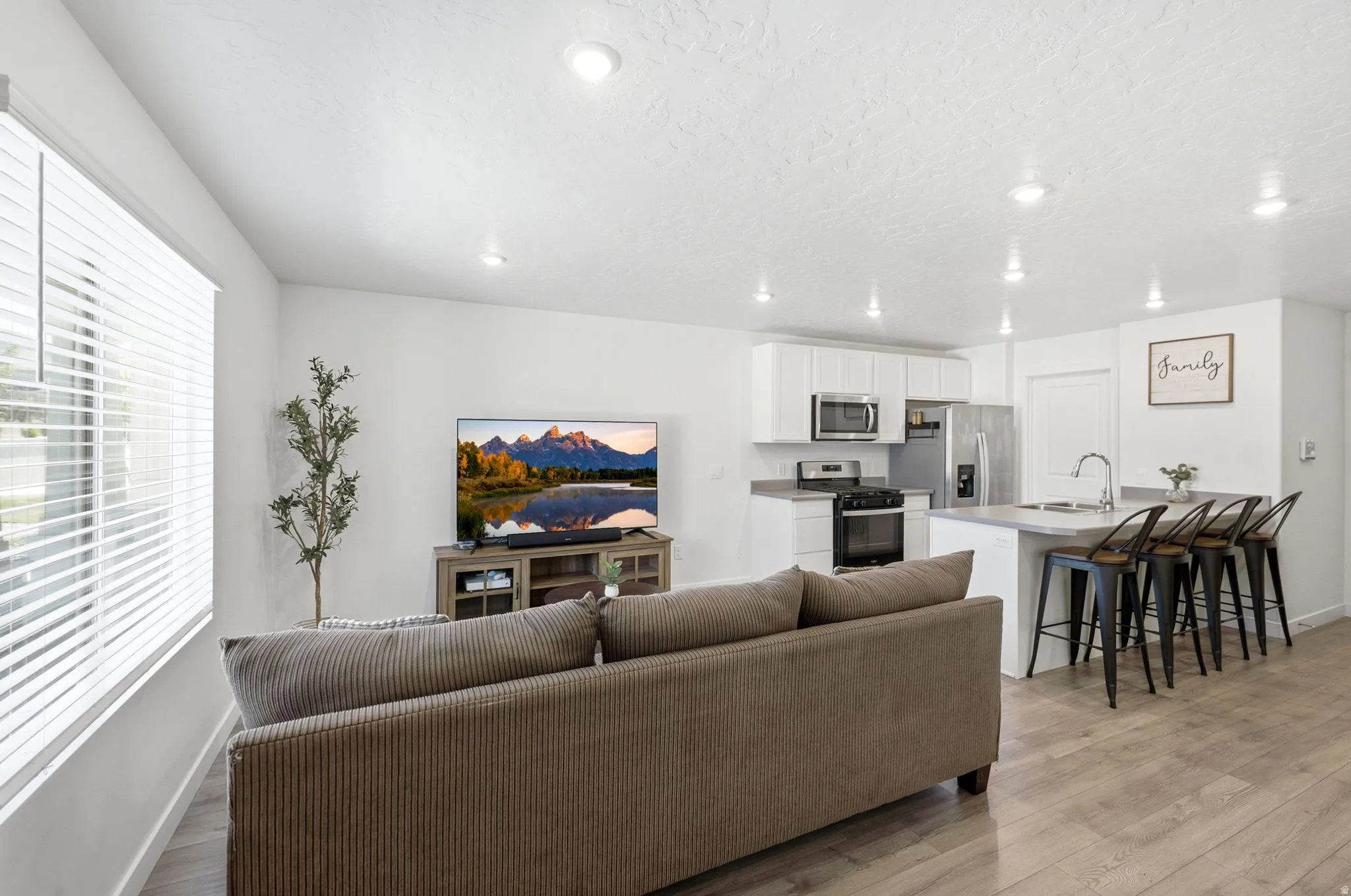 Open-concept living space featuring wood-finish flooring, recessed lighting, and a kitchen island with seating