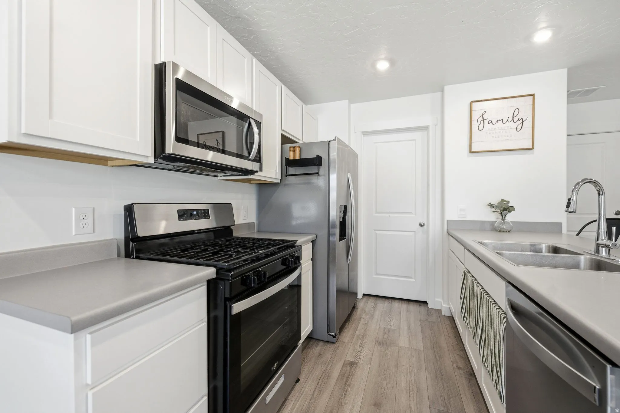 Modern kitchen featuring white shaker cabinetry, stainless steel appliances, gas range, light gray countertops, and wood-finish flooring