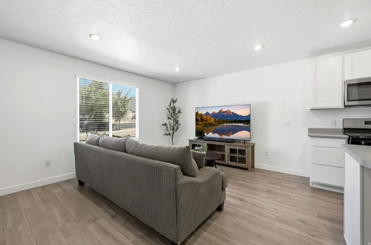 Open-concept living space featuring wood-finish flooring, recessed lighting, a window with blinds, white cabinetry, and a countertop