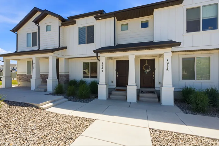 Contemporary townhome exterior featuring white vertical siding, dark trim, a stone accent facade, covered front porches with square columns, and dark entry doors