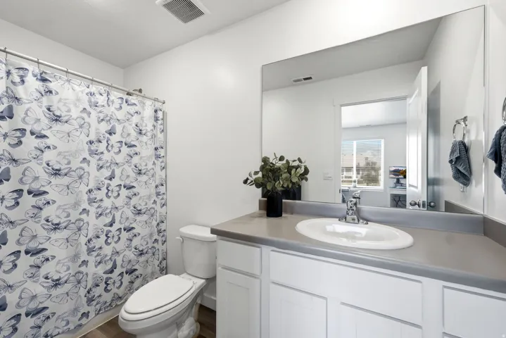 Bathroom featuring a vanity with an integrated sink, a large wall-mounted mirror, white shaker-style cabinetry, and wood-finish flooring
