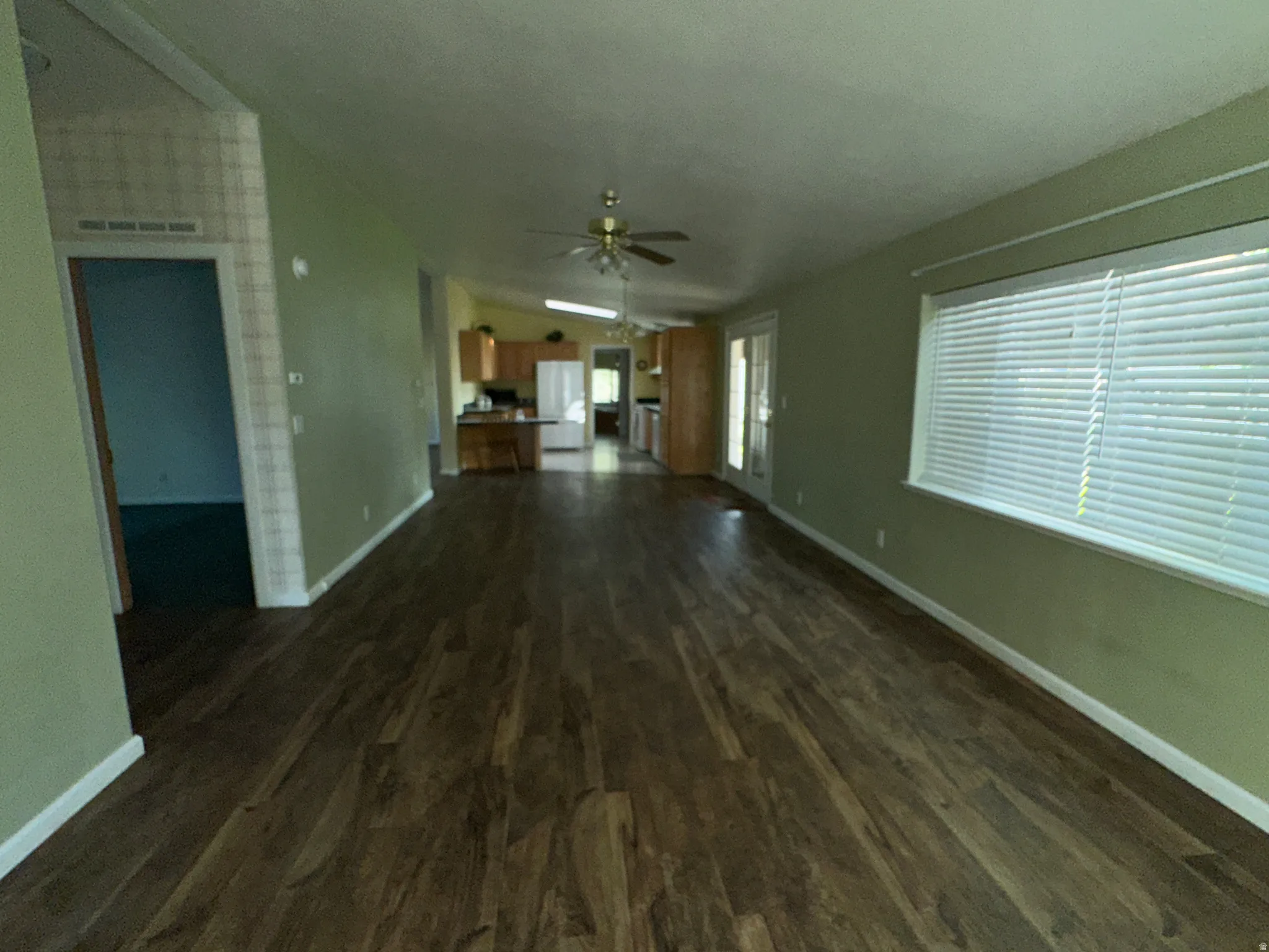Spacious living area featuring wood-finish flooring, a vaulted ceiling, and a large window with blinds