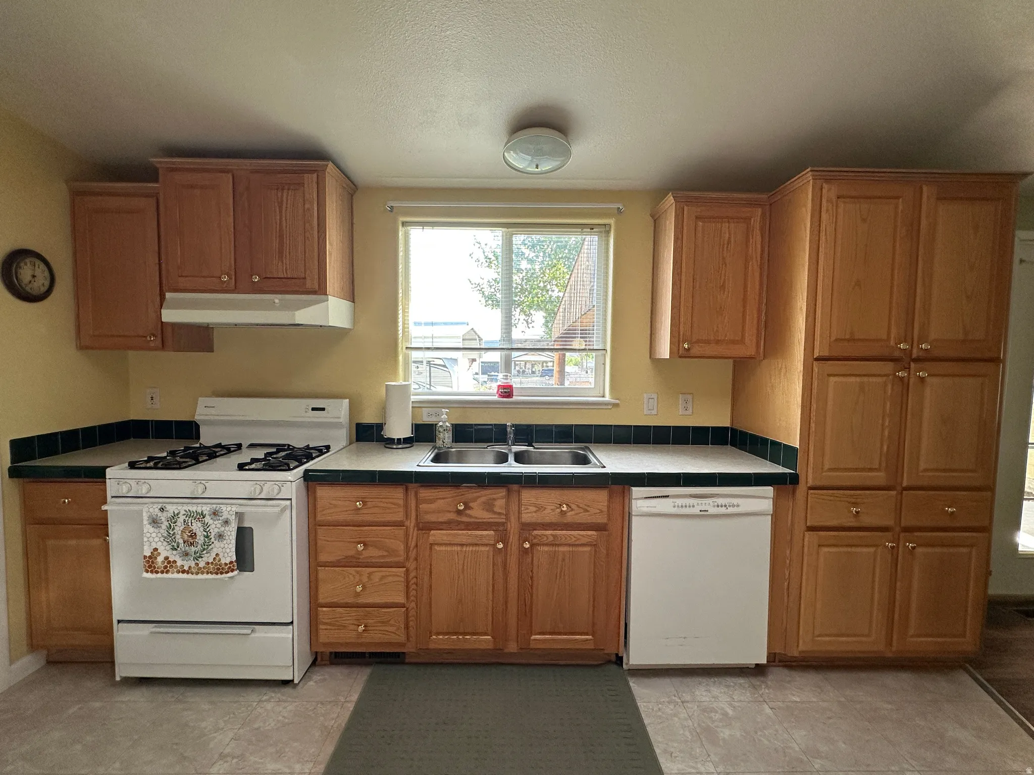 Kitchen featuring ample wood cabinetry, a double basin sink, white appliances, and tiled countertops with a contrasting backsplash